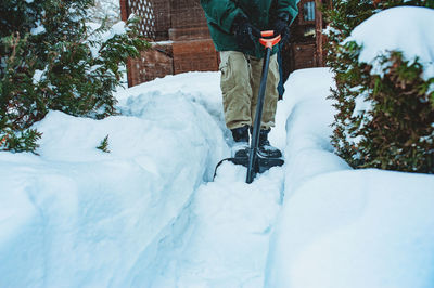 Low section of man removing snow with shovel outside house