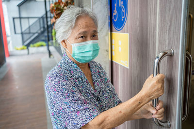 Close-up of senior woman wearing mask standing by door