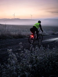 Rear view of man riding bicycle on field against sky during sunset