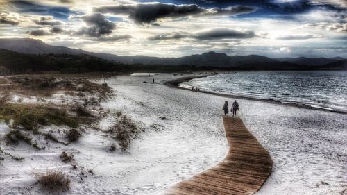 View of calm beach against cloudy sky