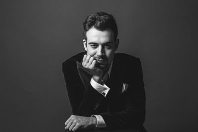 Portrait of young man sitting against black background