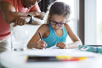 Father looking at daughter drawing on paper at home