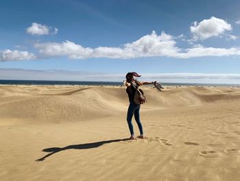 Woman with arms outstretched standing at beach against sky