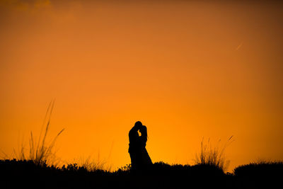 Silhouette woman photographing on field against orange sky