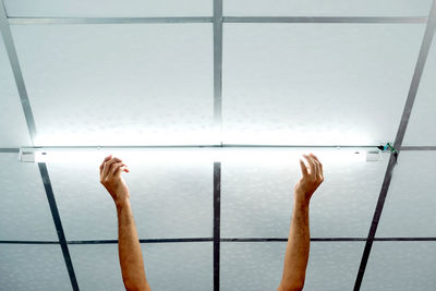 Close-up of a man's hand installing a long led light bulb on the ceiling.