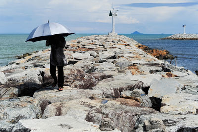 Man with umbrella walking on groyne against sky