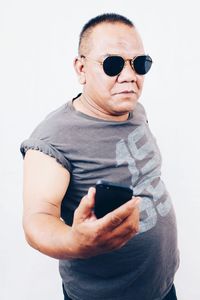 Portrait of mature man wearing sunglasses while standing against white background