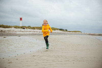 Full length of smiling girl running on beach against sky