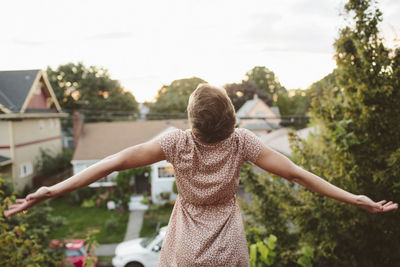 Rear view of woman with arms outstretched standing against plants