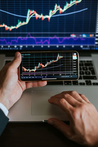 Cropped hands of businessman holding smart phone and using laptop