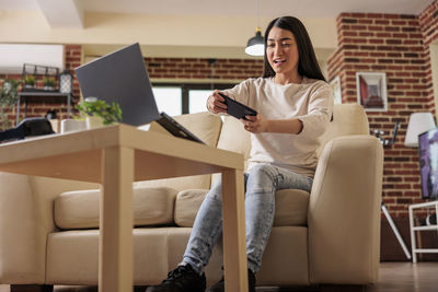 Young woman using mobile phone while sitting on sofa at home