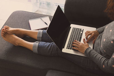 Low section of woman using laptop while sitting on sofa in living room at home