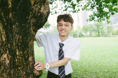 Portrait of young man standing on tree trunk