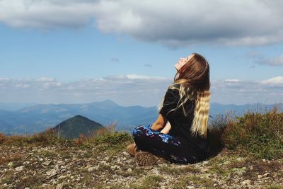 Woman sitting on mountain against sky