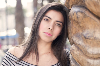 Portrait of beautiful young woman standing on tree trunk