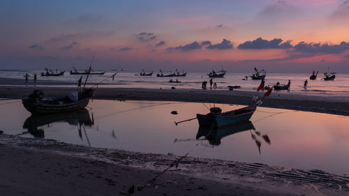 Fishing boats moored at beach against sky during sunset