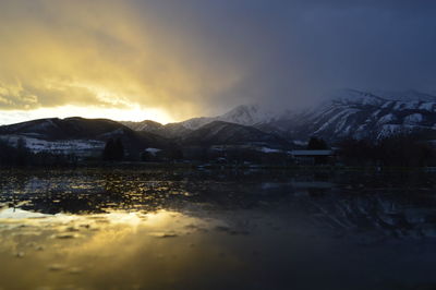 Scenic view of lake by snowcapped mountains against sky during sunset