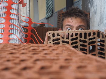 Portrait of shocked young man hiding behind brick