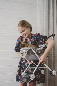 Side view of girl in clover dress holding cat sitting in stroller at home