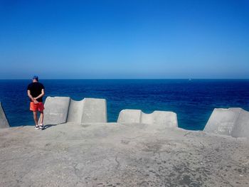 Rear view of man standing on beach against clear blue sky