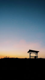 Silhouette windmill on field against clear sky during sunset