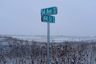 Road sign on snow covered landscape against clear sky