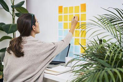 Young woman with laptop on desk working with adhesive notes on the wall