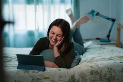 Young woman using phone while relaxing on bed at home