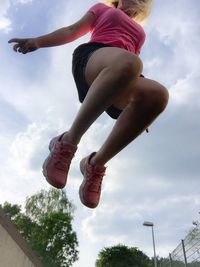 Low angle view of woman jumping against sky