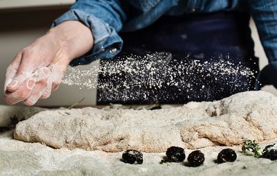 Midsection of person spreading flour on dough in bakery