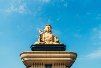 Low angle view of buddha statue against blue sky