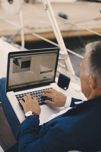 High angle view of senior man using laptop while sitting on yacht