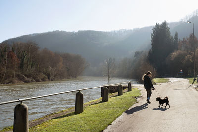 Rear view of girl walking with dog by the river