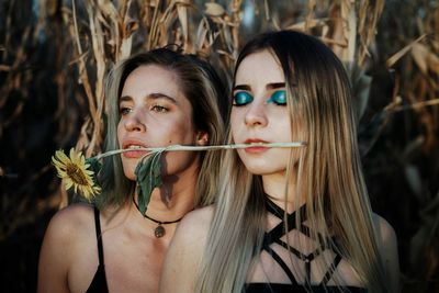 Beautiful woman with flower in mouth against plants