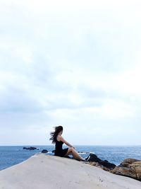 Woman sitting on beach by sea against sky