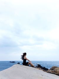 Woman sitting at beach against cloudy sky