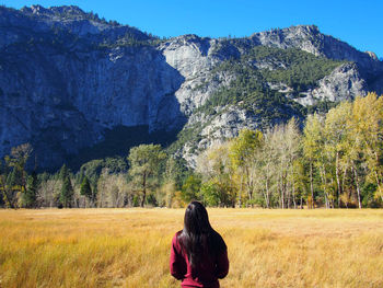 Woman standing in field looking at mountain range against blue sky