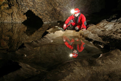 Spelunker wondering inside an underground cave hall with a small water pond