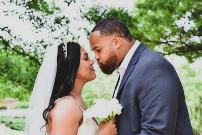 Side view of couple holding hands while standing against trees