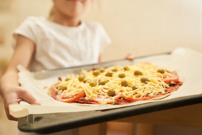 The girl holds on a baking sheet prepared for baking healthy gluten-free pizza with beef. 