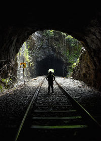 Rear view of boy walking on railroad tracks in tunnel