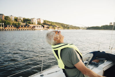 Senior man laughing in boat against sky on sunny day