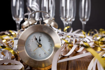 Close-up of alarm clock with decorations and wineglasses on table against black background