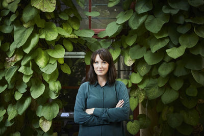 Portrait of confident female architect standing against creeper plants in backyard