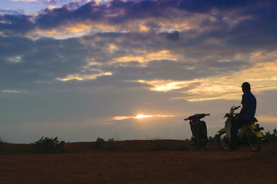 Man with motor scooter on field against cloudy sky during sunset