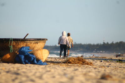 Rear view of men walking at beach against clear sky