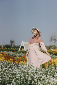 Woman standing by flowering plants on field against sky