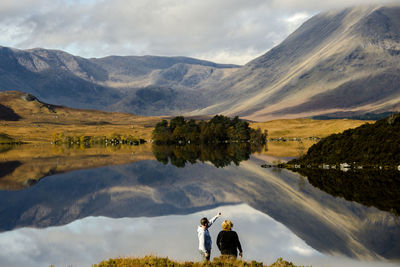 People on lake by mountains against sky