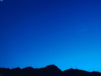 Low angle view of silhouette mountain against clear blue sky