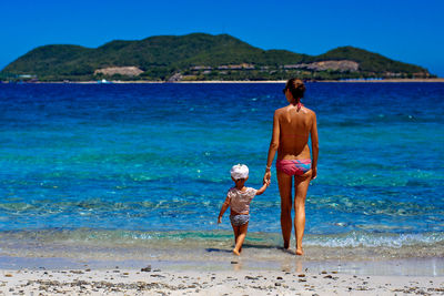 Rear view of friends standing on beach against clear sky